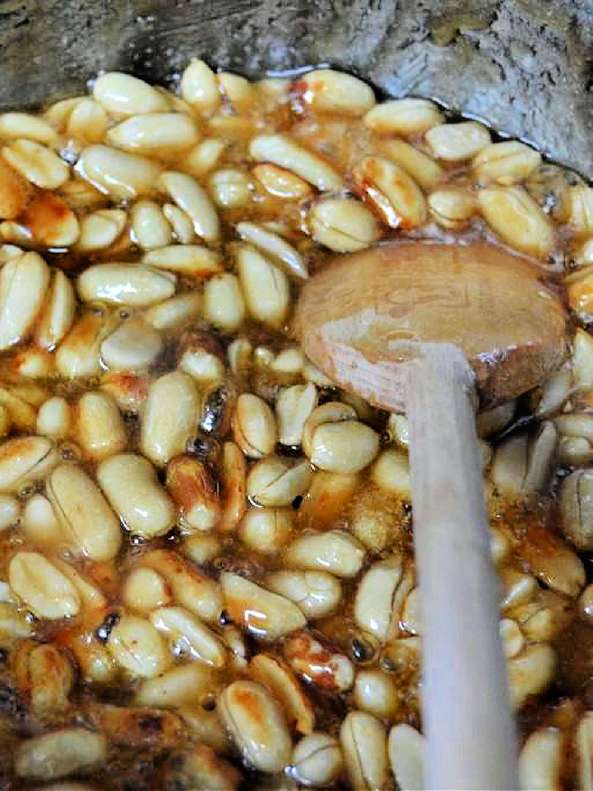 A wooden spoon stirring peanut brittle in a pot.
