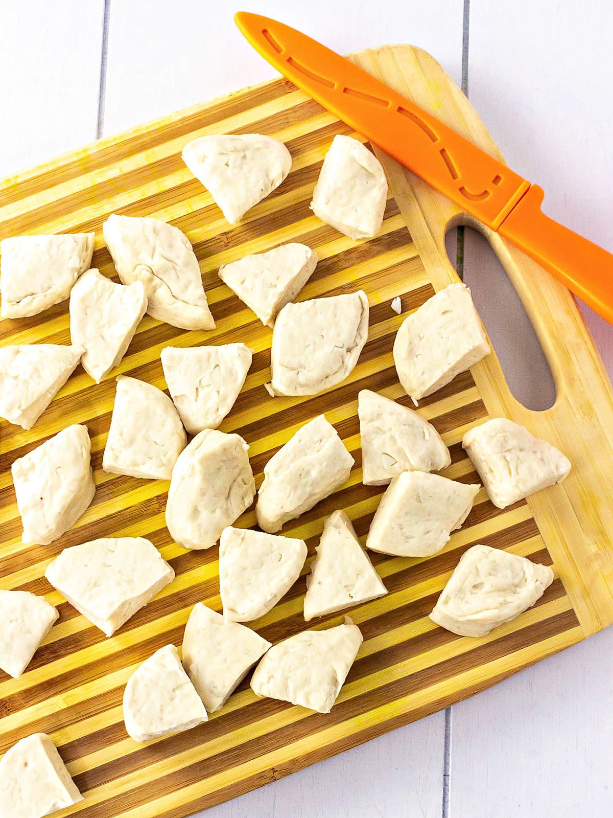 Biscuits cut into quarters on a cutting board with a knife.