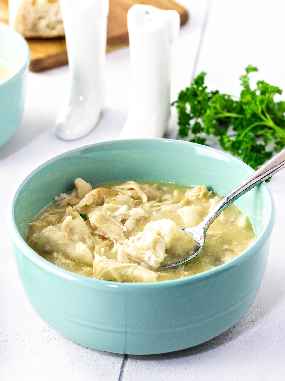 Green bowl with chicken and dumplings and a spoon.