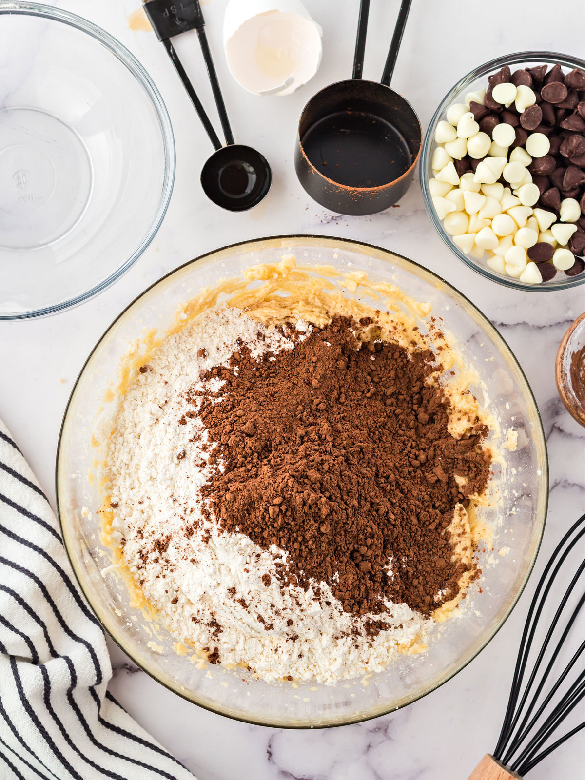 Flour and cocoa powder being added to creamy sugar cookie base in a glass bowl.