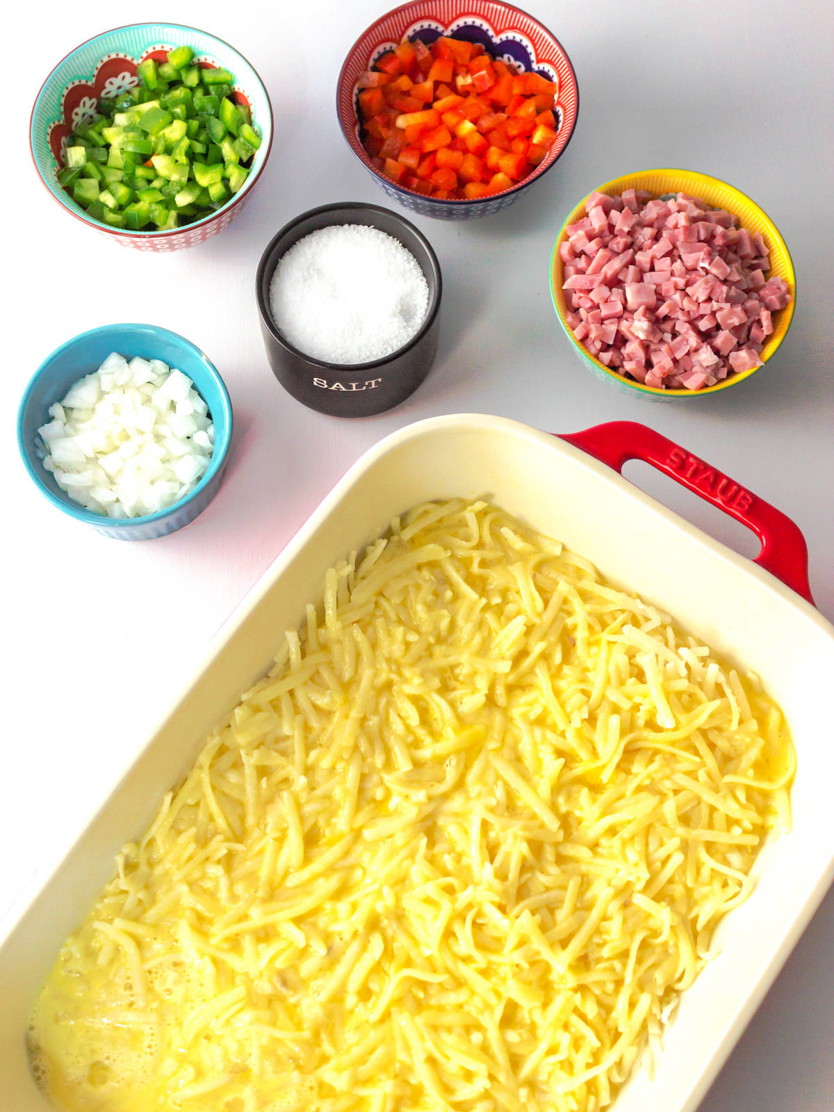 Potatoes in a baking dish and bell peppers, onion, and ham in bowls.