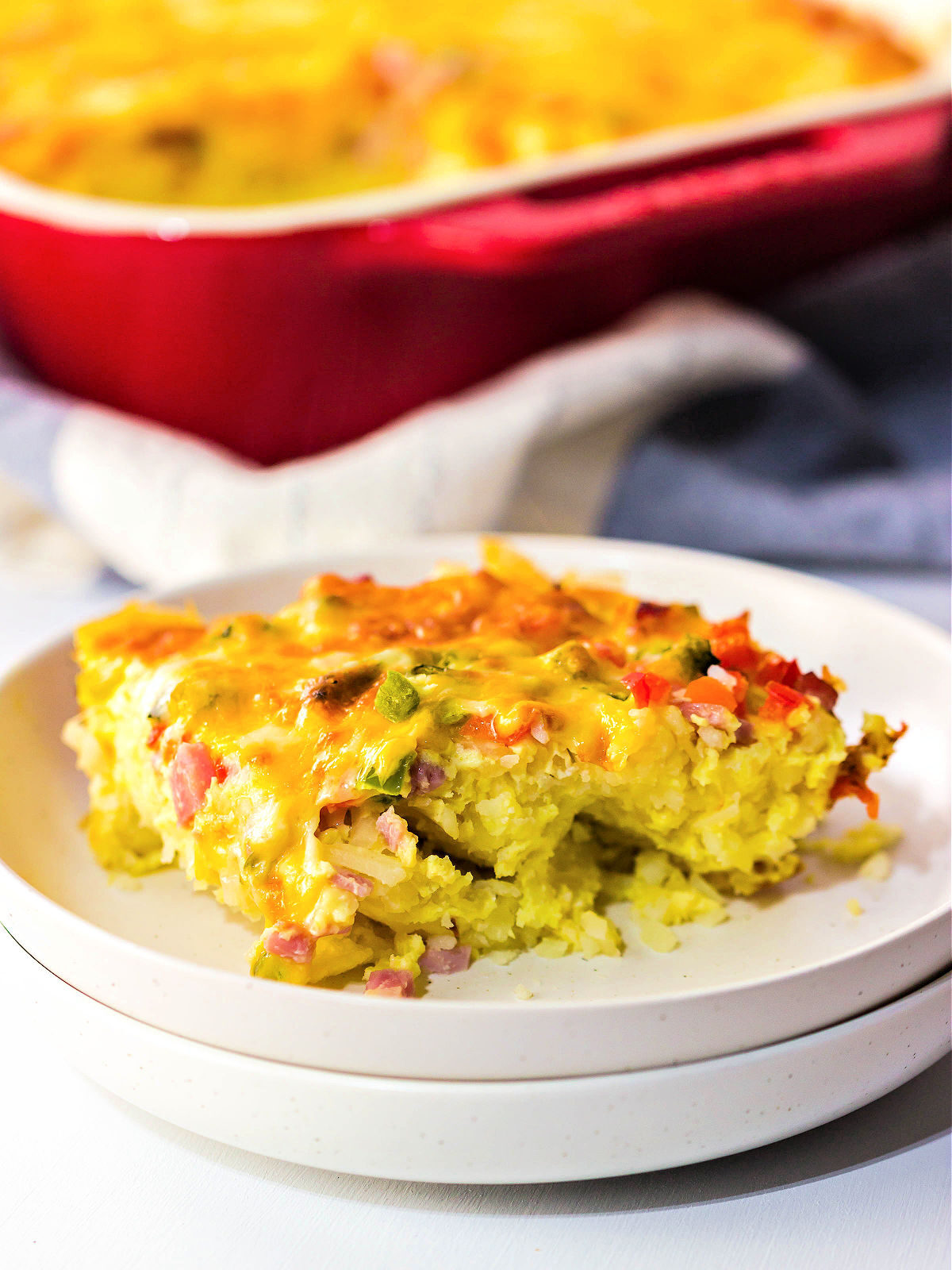 Cheesy breakfast casserole with ham, bell peppers, and onions on a plate.