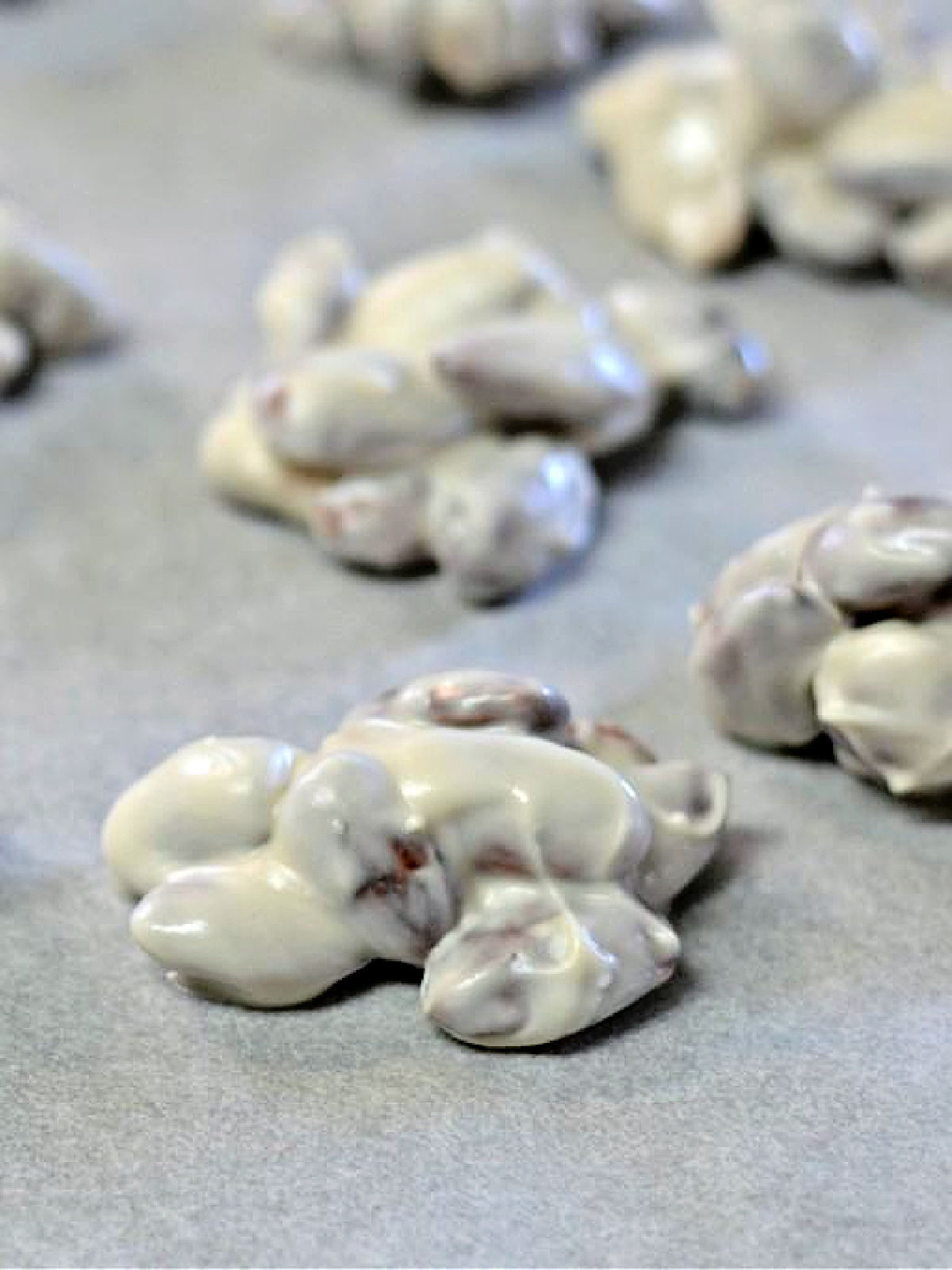 Almonds covered in white almond bark on parchment paper.