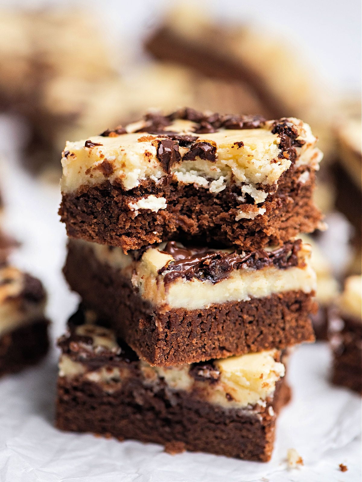 Stack of three cheesecake brownies topped with chocolate chips.