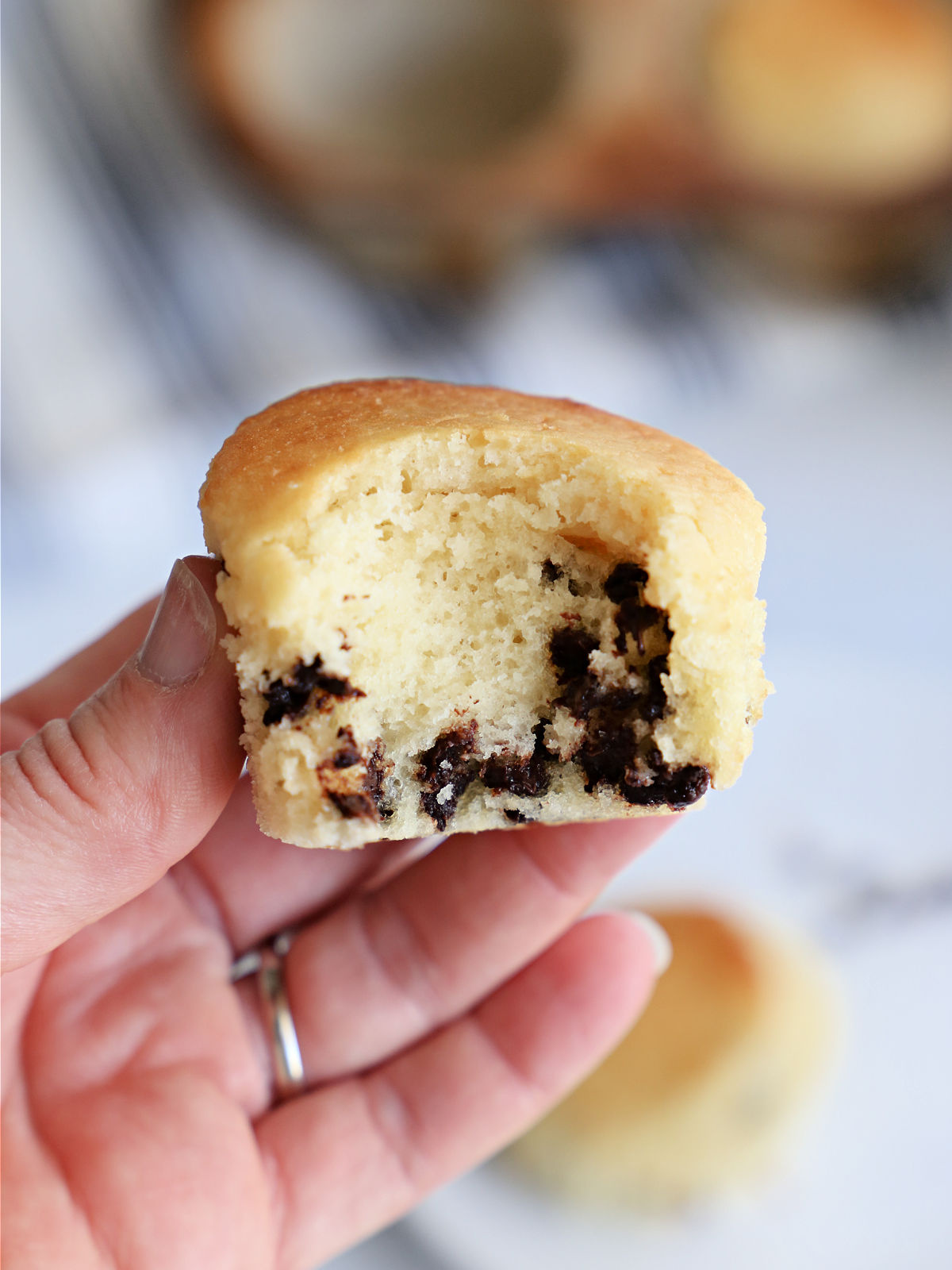 Woman's hand holding a chocolate chip muffin that has had a bite taken out of it.