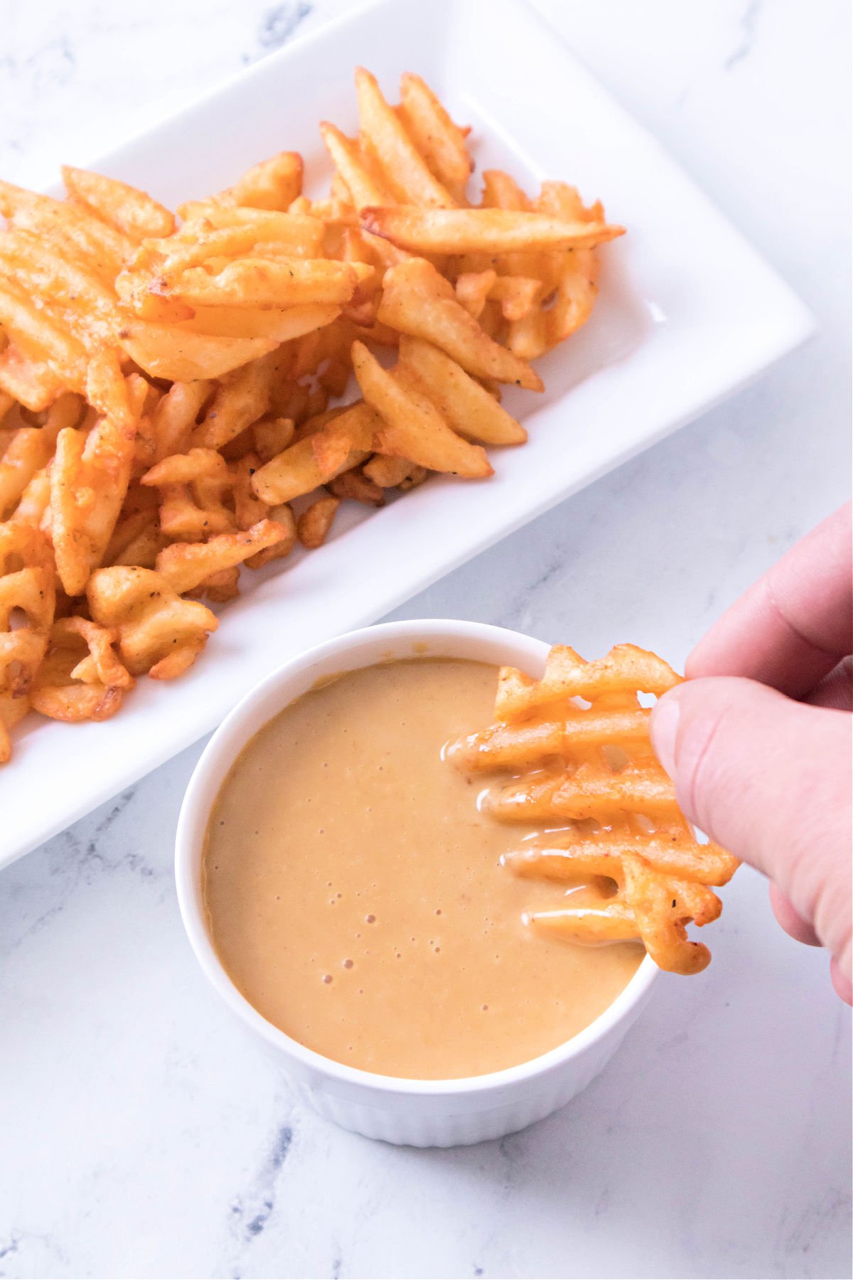 Person dipping a crinkle cut French fry into homemade Chick-Fil-A sauce.