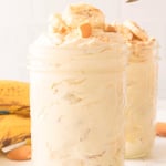 Jars of banana pudding topped with bananas and crushed vanilla wafers.