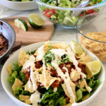 Taco salad with lime wedges and drizzled with Ranch dressing.