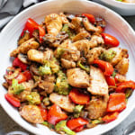 Bowl of Cajun chicken with red bell peppers and broccoli.