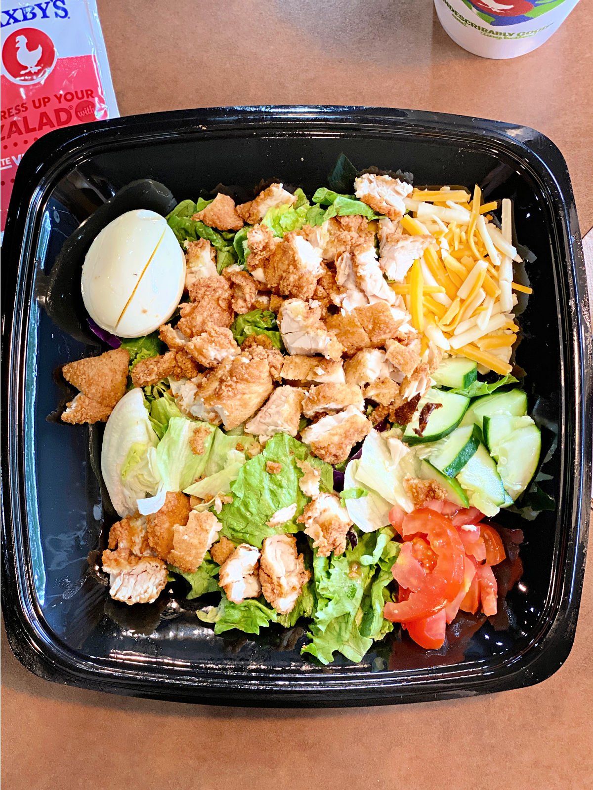 Cobb salad with fried chicken, hard boiled egg, cheese, cucumbers, and tomatoes.