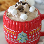 Red mug filled with chocolate dip topped with chocolate chips and marshmallows.