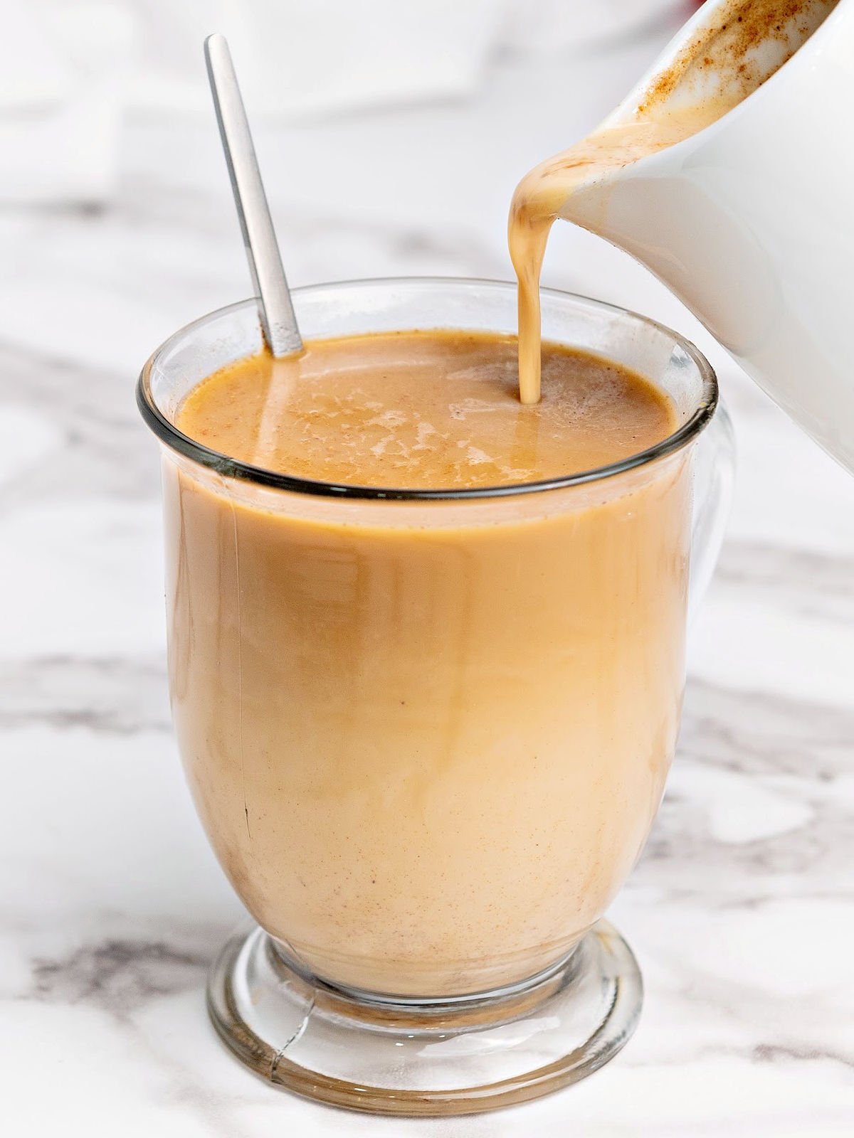 Pumpkin spice creamer being poured into a cup of coffee.
