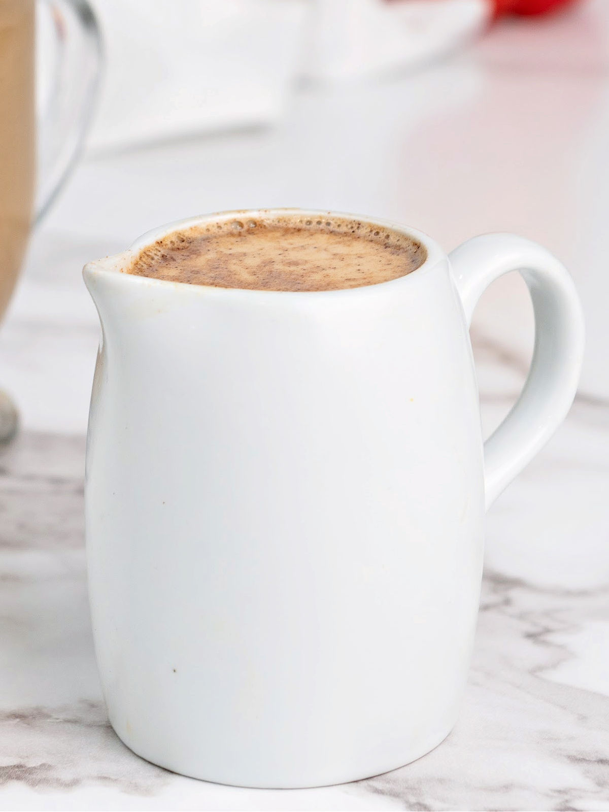 Small white pitcher filled with coffee creamer.