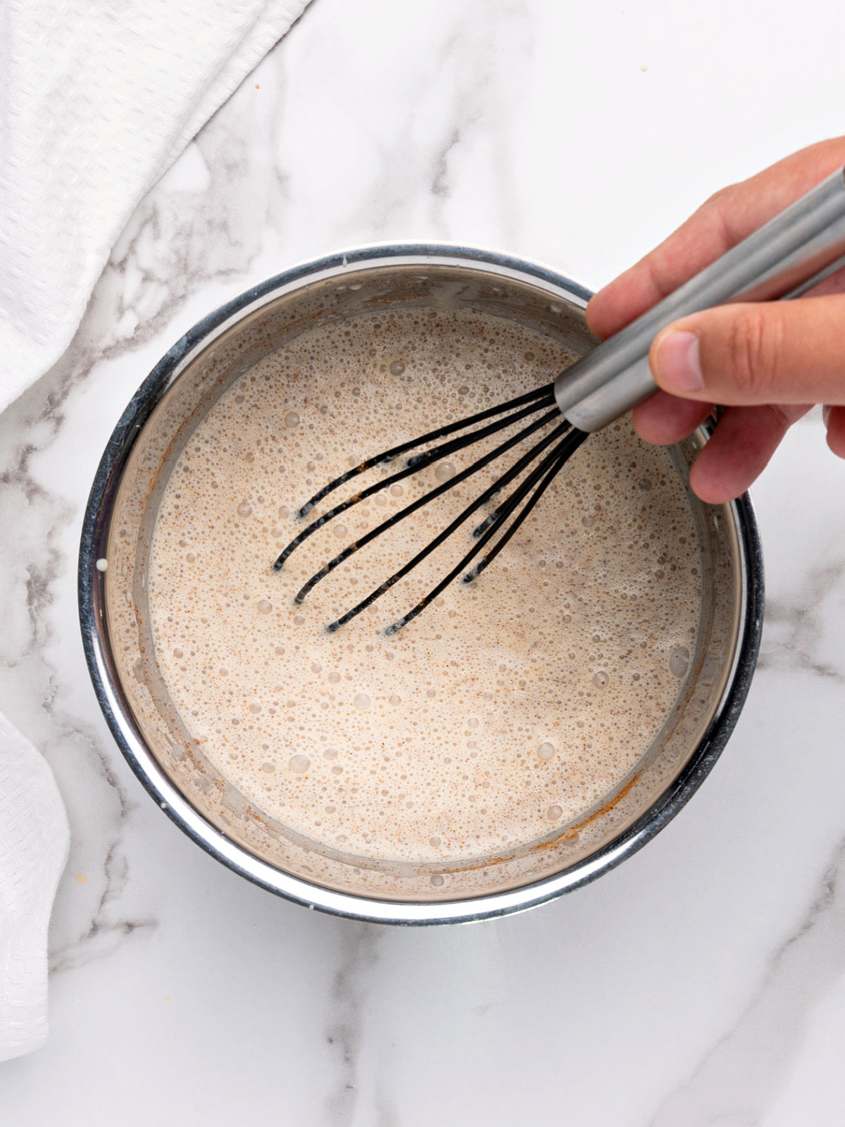 Hand whisking ingredients in a small pot.