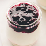 Jar of cheesecake topped with blueberry pie filling.
