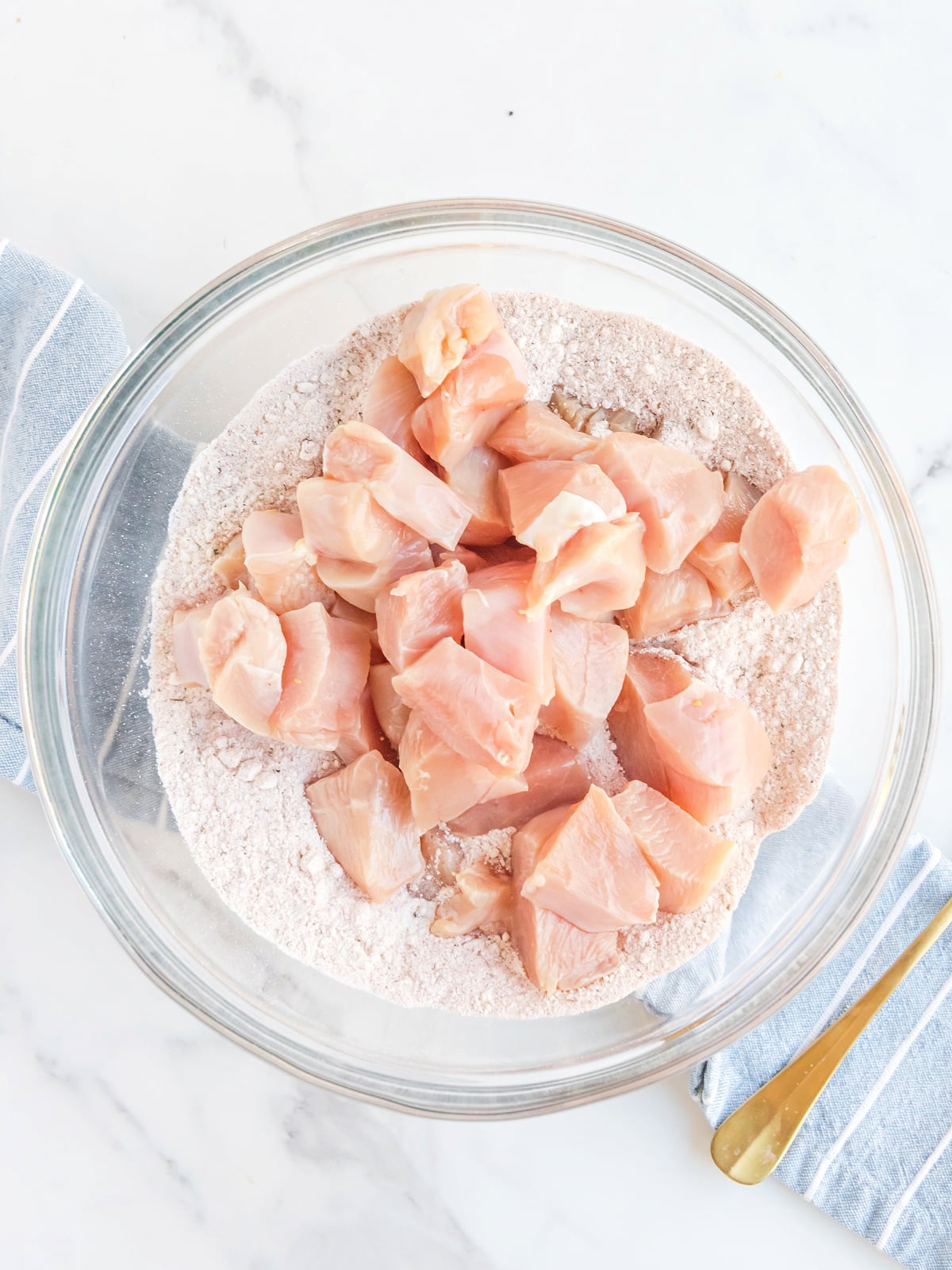 Chicken pieces on top of flour mixture in a glass bowl.