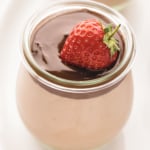 Jar of chocolate cheesecake topped with ganache and a strawberry.