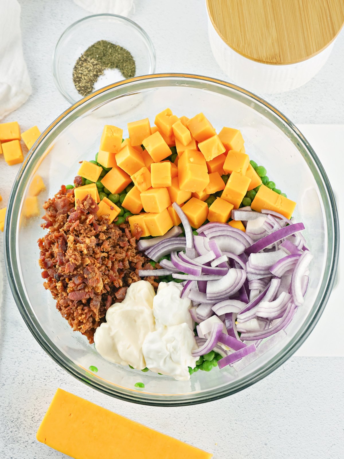 Cheddar cheese, bacon, red onion, peas, sour cream, and may in a mixing bowl.
