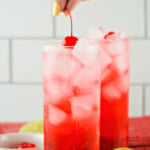 Woman's hand placing a cherry on top of a mocktail.