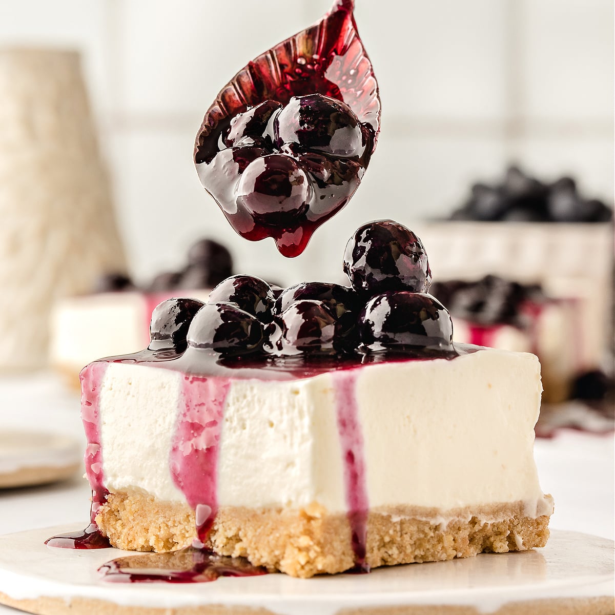 Blueberry sauce being spooned over a slice of cheesecake.