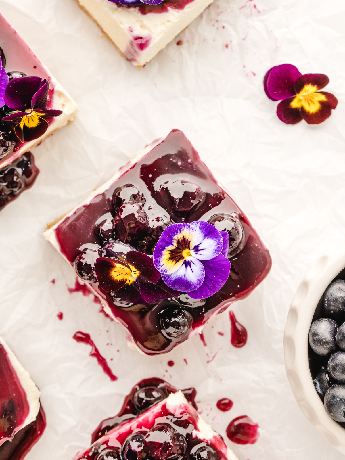 Slice of blueberry cheesecake with an edible flower on top.