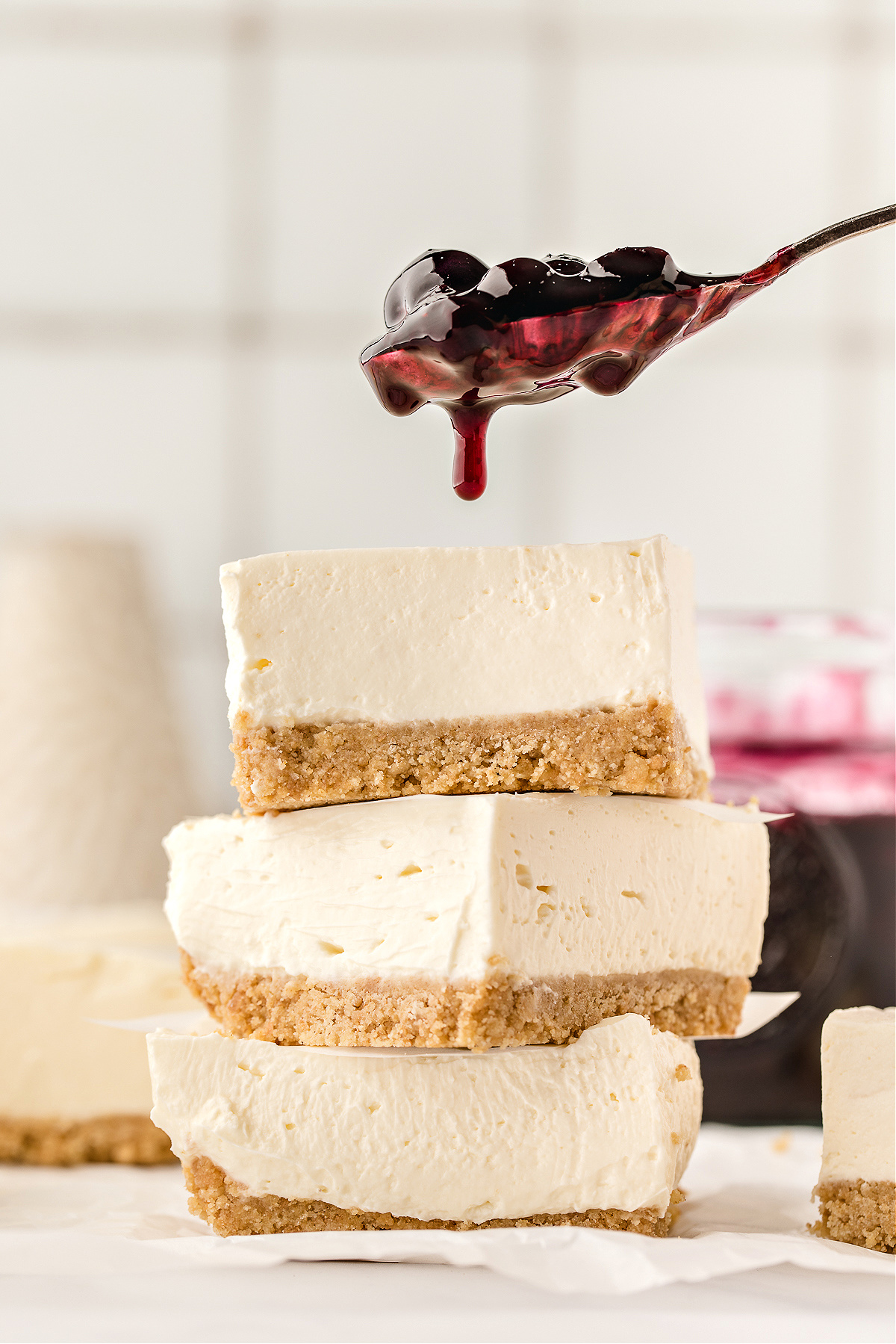 Stack of cheesecake slices being topped with blueberry sauce.