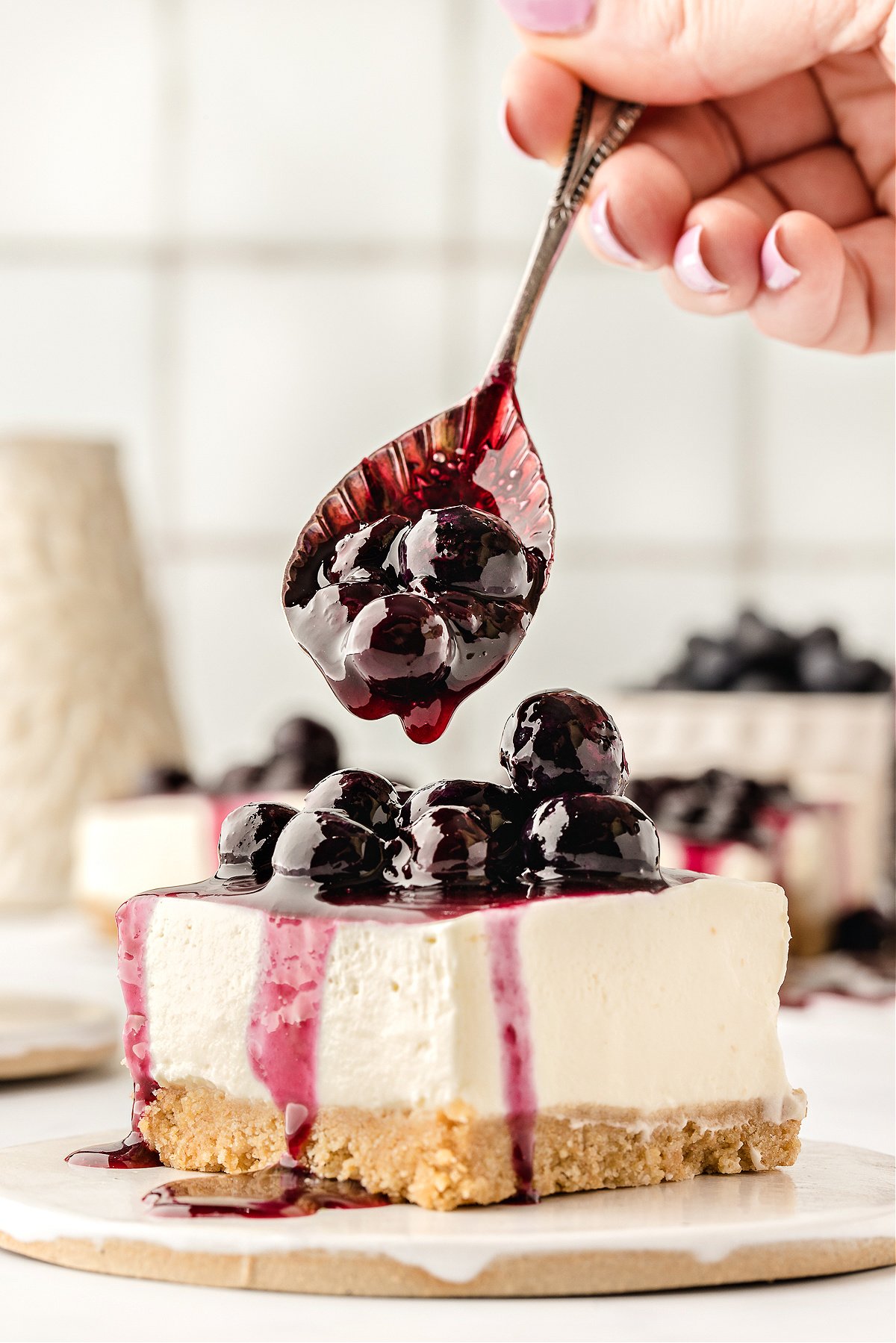 Blueberry sauce being spooned over a piece of cheesecake.