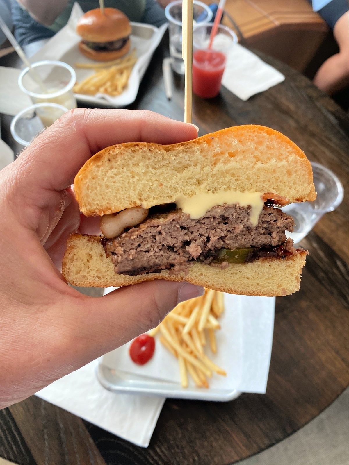 Half a hamburger on a brioche bun in front of a plate with French fries.