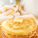 Syrup being poured over a stack of pancakes.