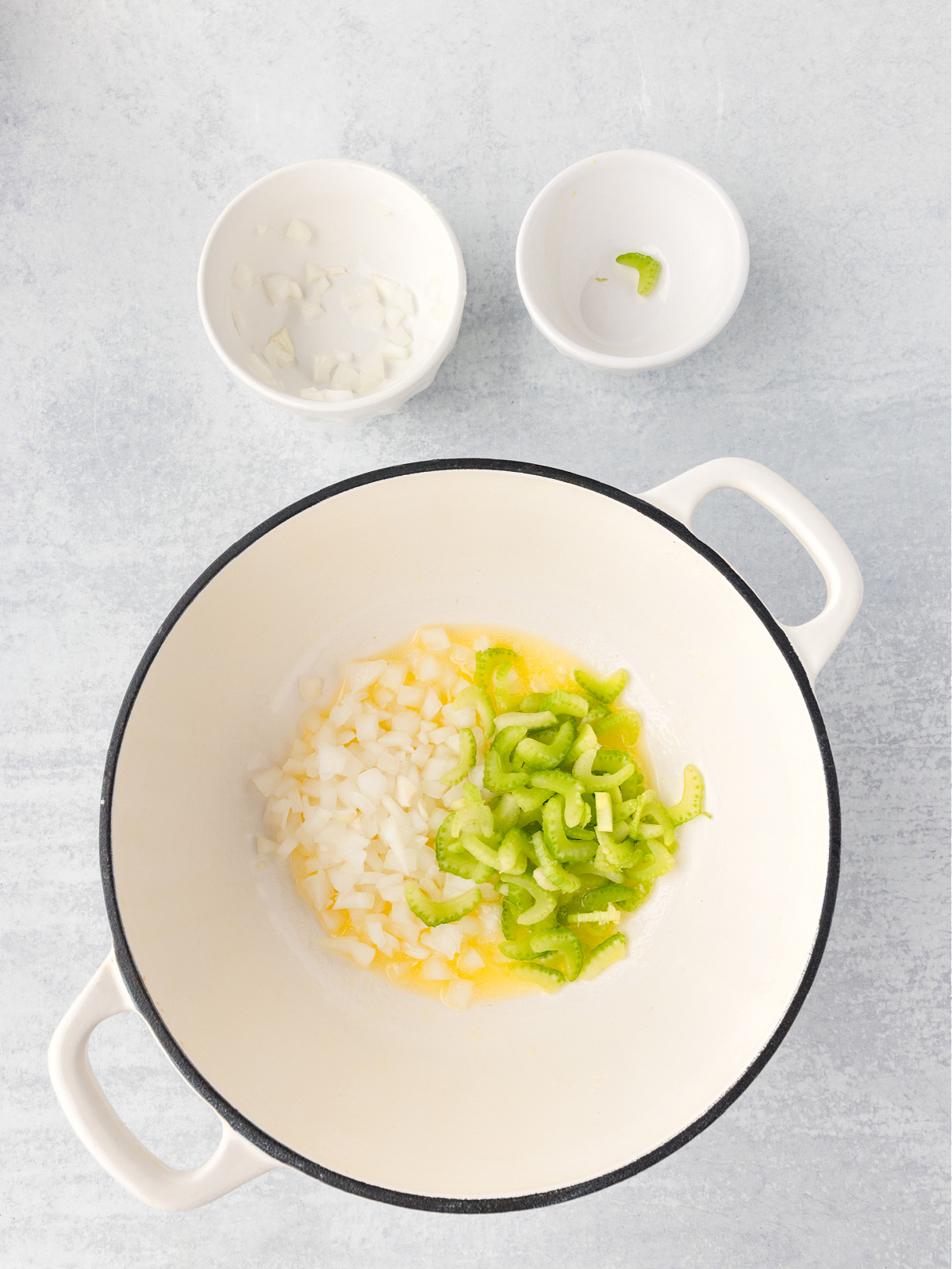 Celery and onions on top of melted butter in a pot.
