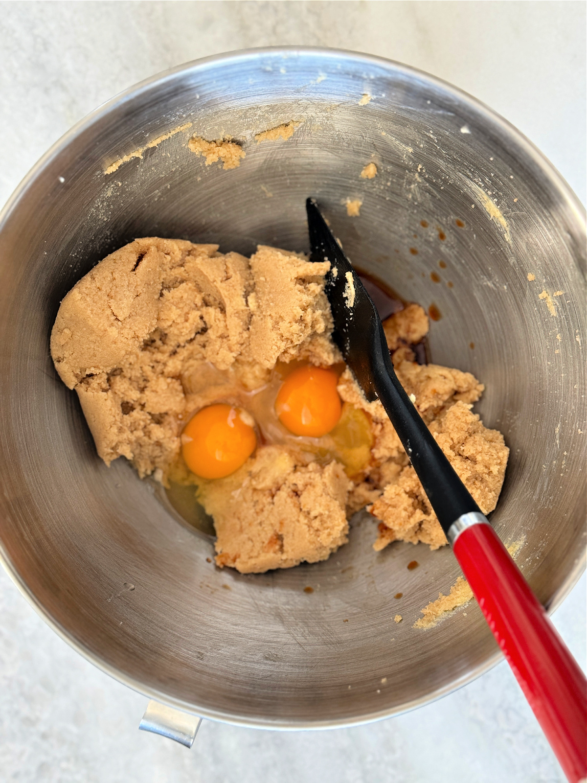 Two eggs being added to a sugar and butter mixture in a mixer.