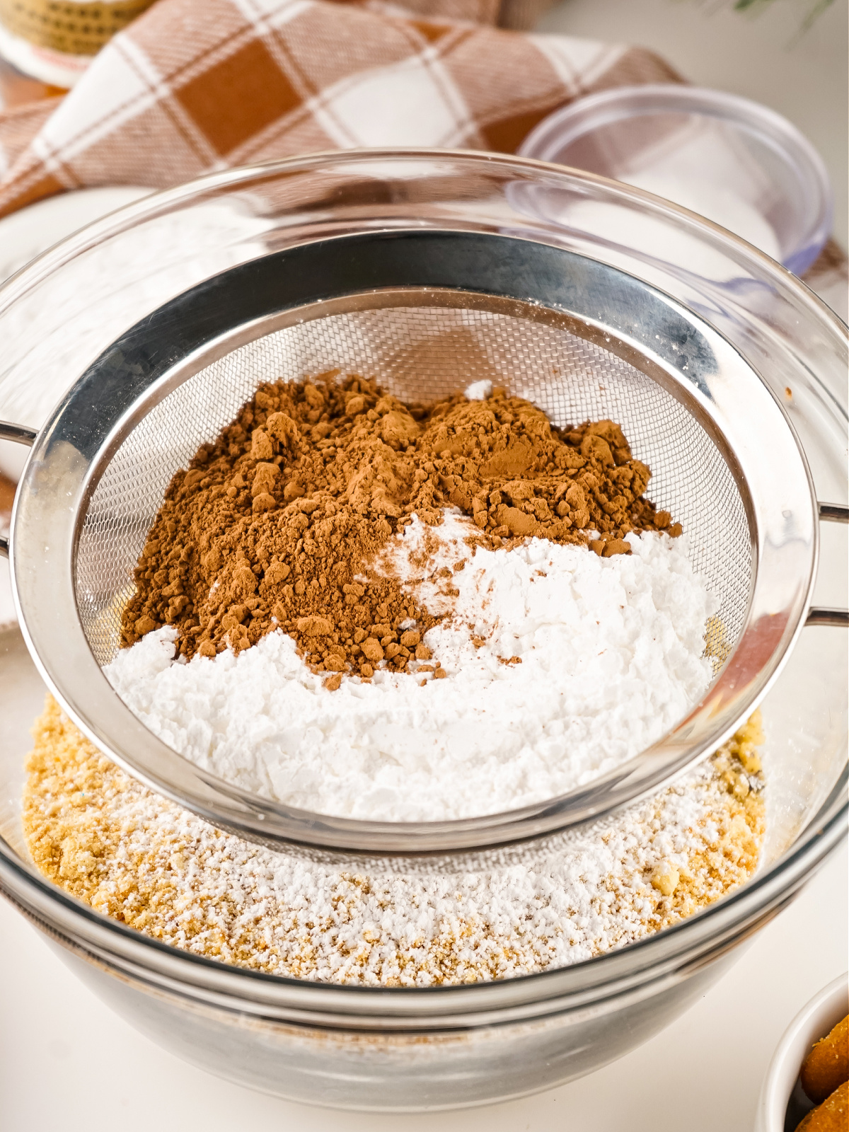 Cocoa powder and powdered sugar being sifted into a bowl.