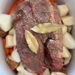 Seasoned pot roast on top of vegetables in a Crockpot and topped with two bay leaves.