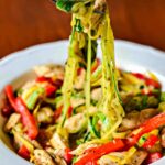 A fork with a bite of honey garlic chicken and veggie noodles.