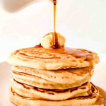 Maple syrup being poured over a stack of pancakes.