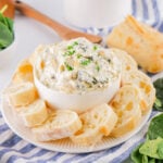 Bowl of spinach artichoke dip surrounded by small slices of French bread.
