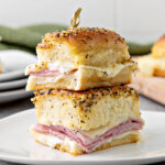 Stack of two ham and cheese sliders with a wooden toothpick in the center holding them in place.