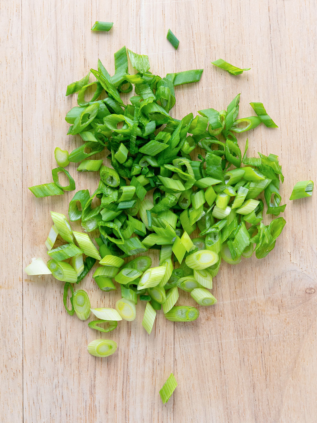 Freshly sliced green onions on a wooden cutting board.