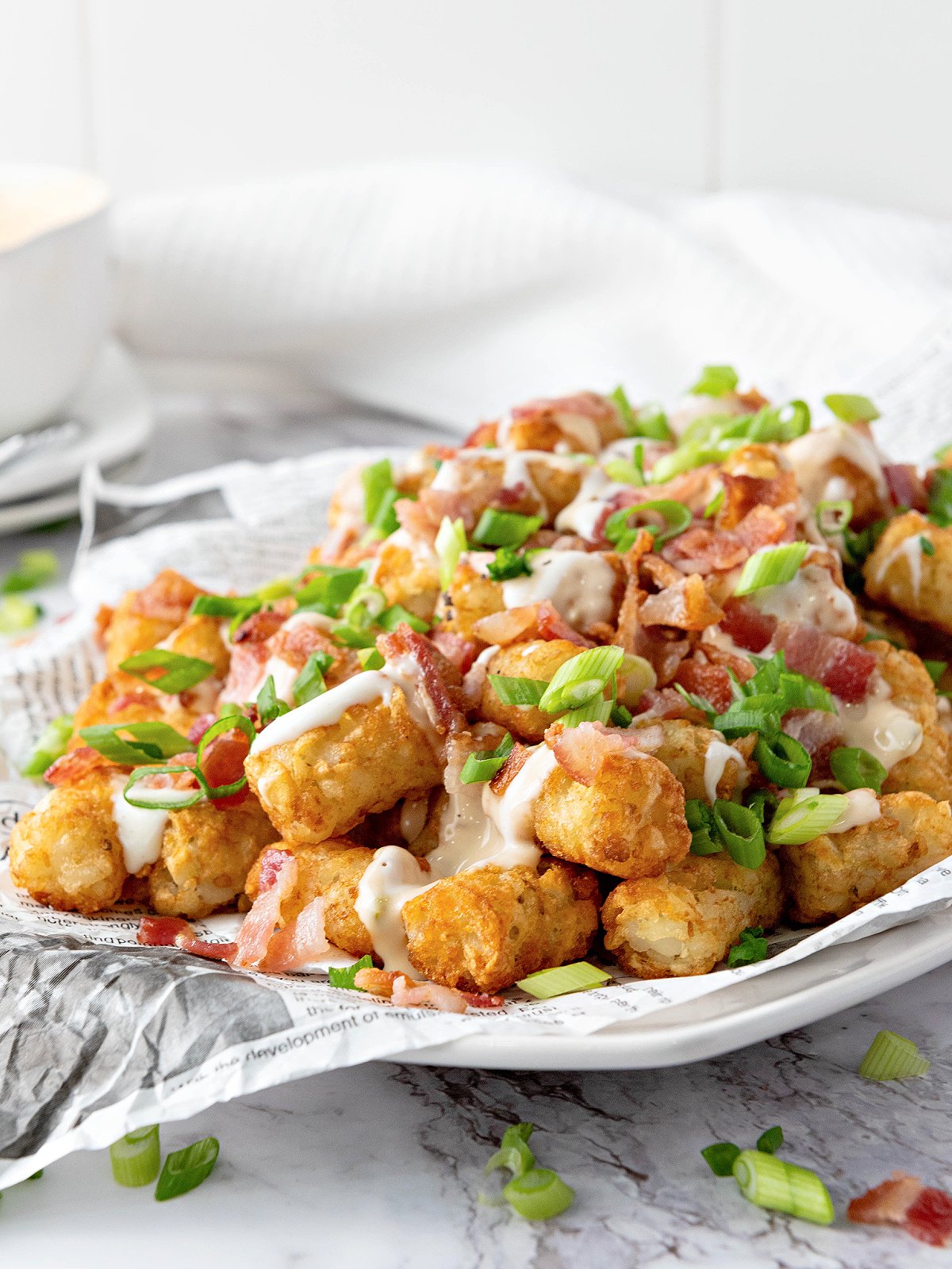 Plate of tater tots covered with Ranch dressing, queso, bacon, and green onions.