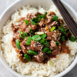 Bowl of white rice topped with beef mixture and green onions and sesame seeds.