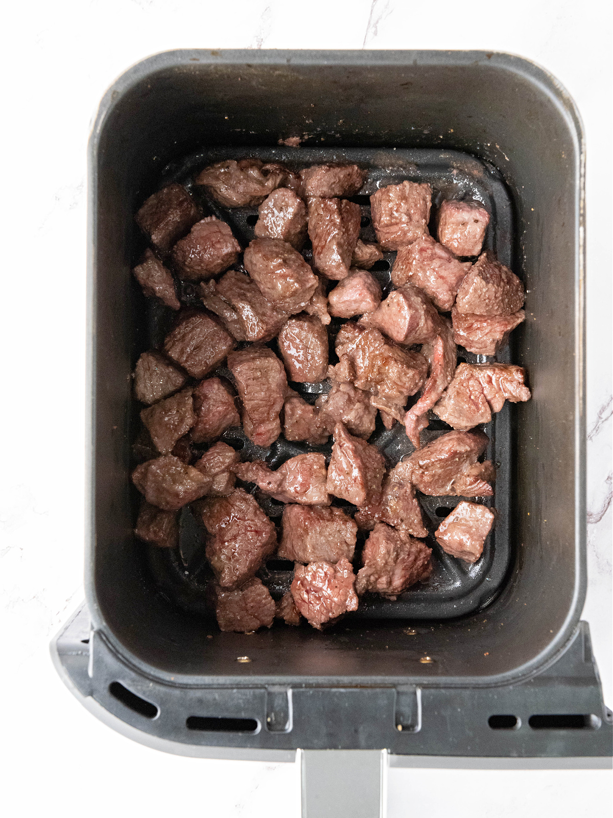 Cooked steak bites in an air fryer basket.