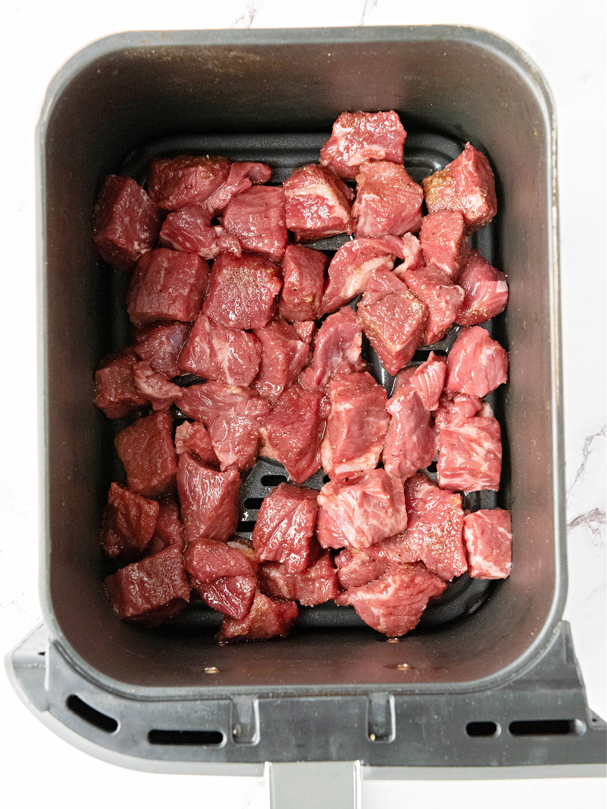 Seasoned steak bites in the basket of an air fryer.