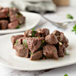 Plate of steak bites covered in a garlic, parsley, and melted butter mixture.