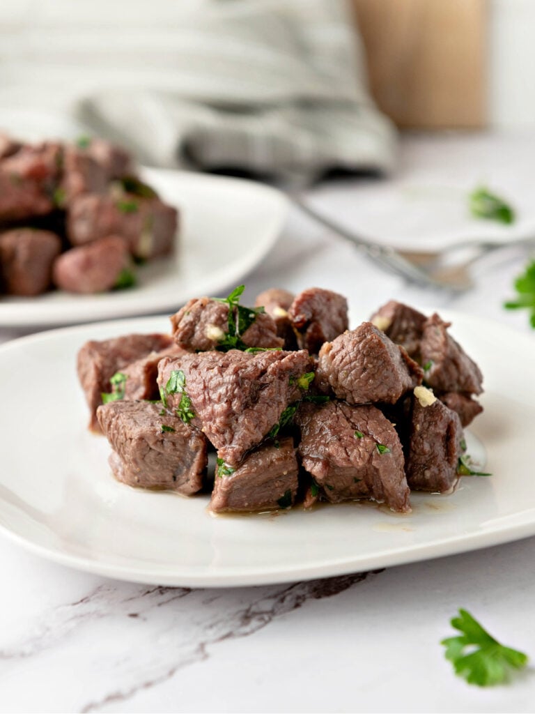 Plate of steak bites covered in a garlic, parsley, and melted butter mixture.