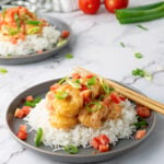 Plate of rice topped with Bang Bang Shrimp, green onions, and diced tomatoes.