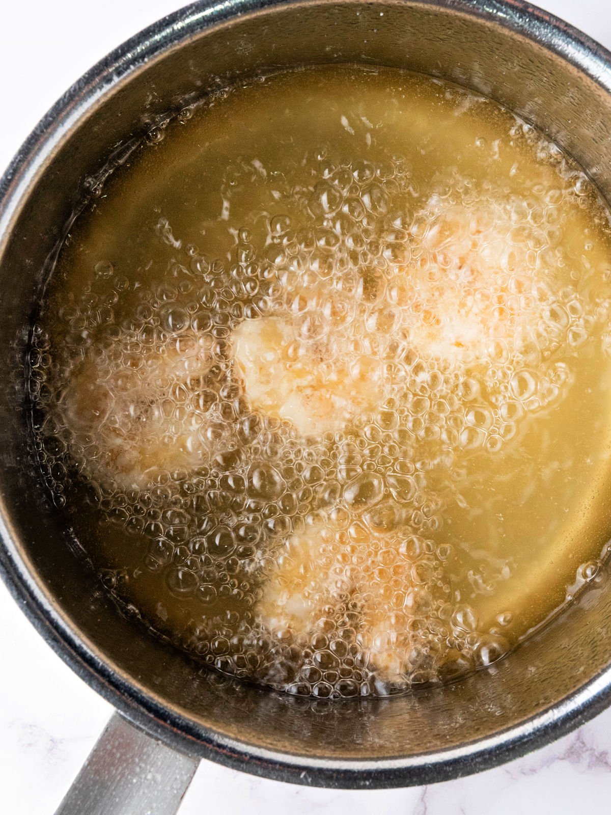 Shrimp frying in hot oil in a skillet.