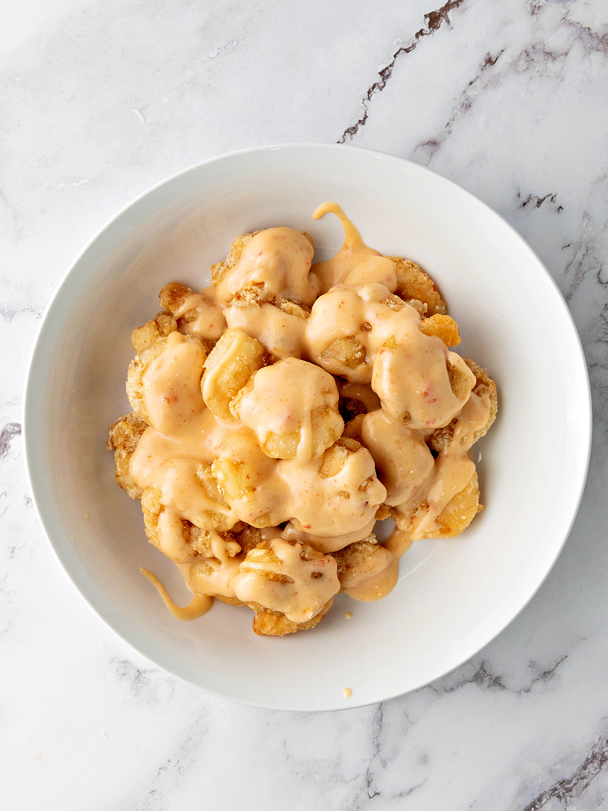 Fried shrimp tossed in bang bang sauce in a mixing bowl.