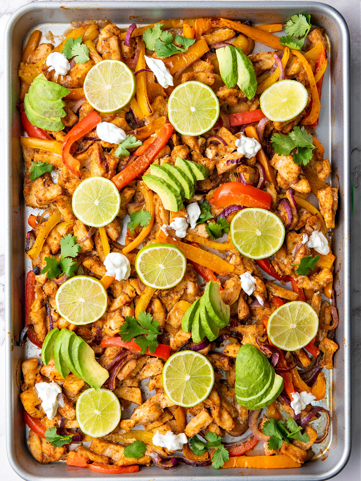 Baked chicken fajitas topped with avocado, lime, cilantro, and sour cream.