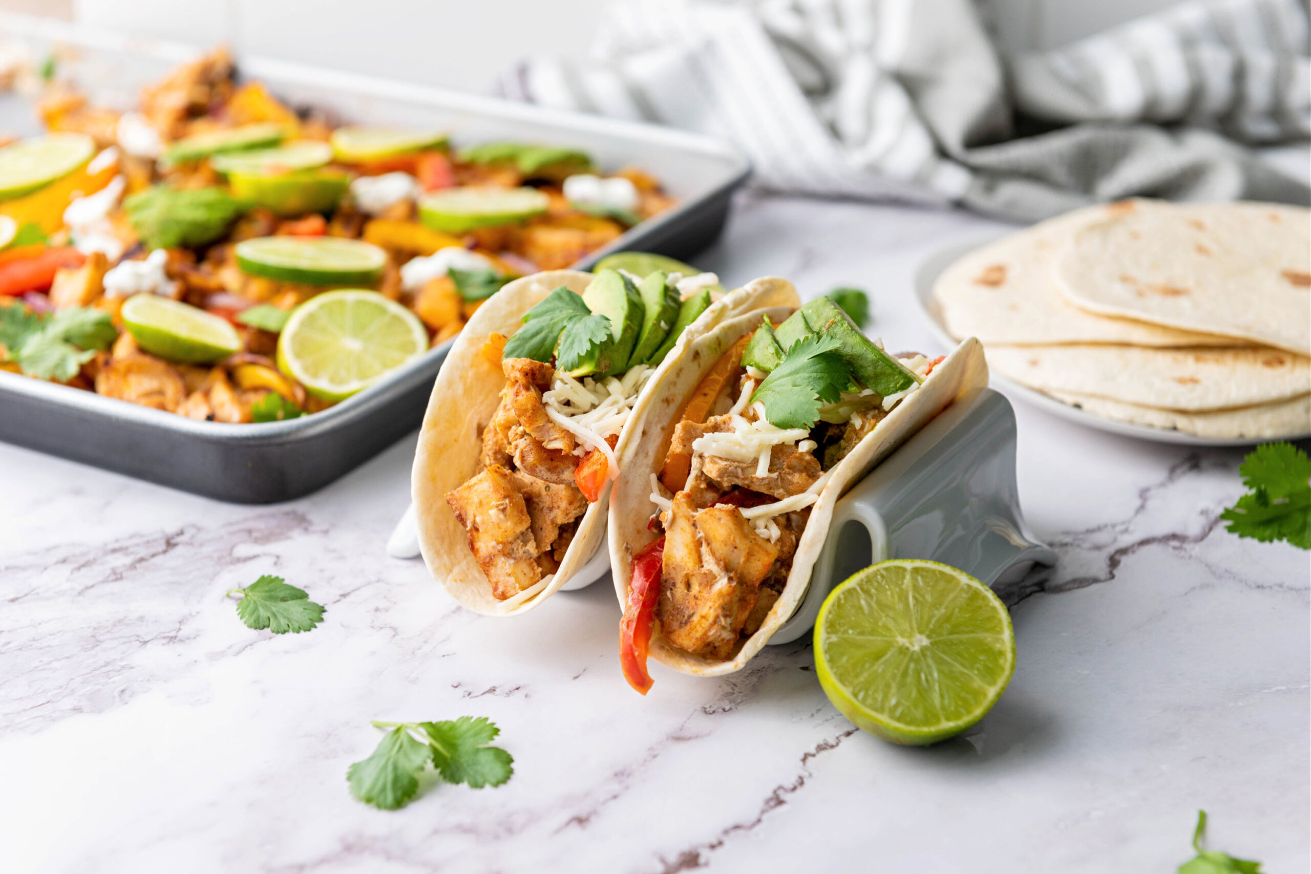 Chicken fajitas on a counter with half of a lime and plate of tortillas.