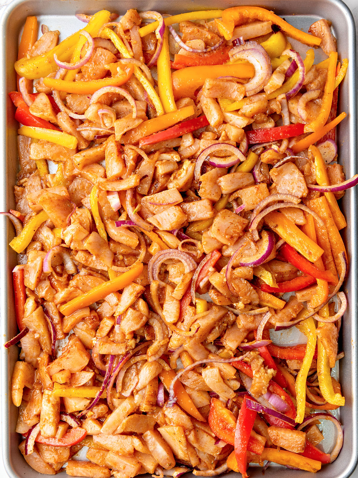 Seasoned raw chicken and vegetables on a baking sheet.
